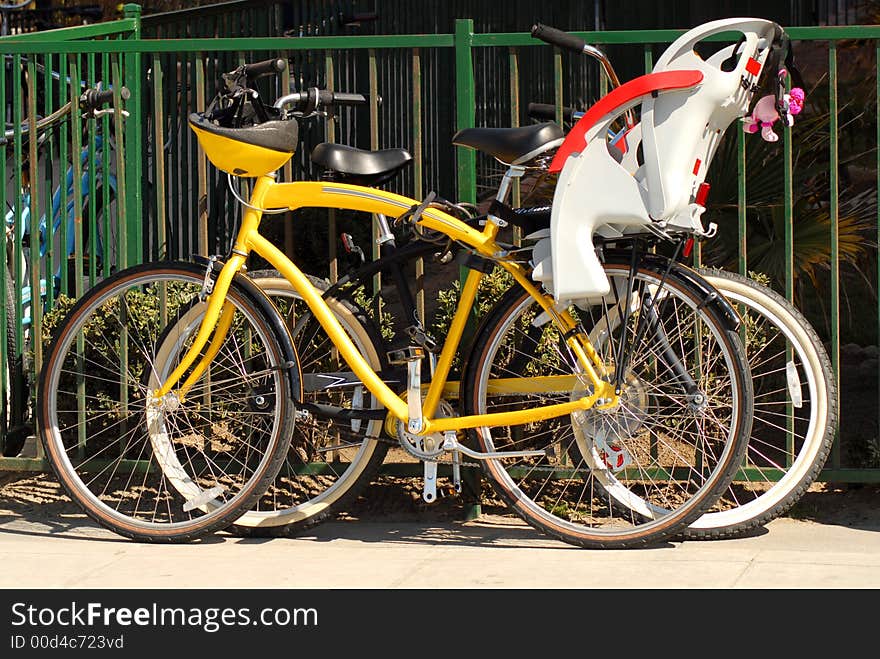 Two bicycles resting against a fence on the sidewalk