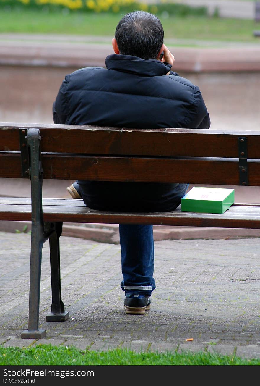 A young man is making  call in park, sitting on a bench. A young man is making  call in park, sitting on a bench.