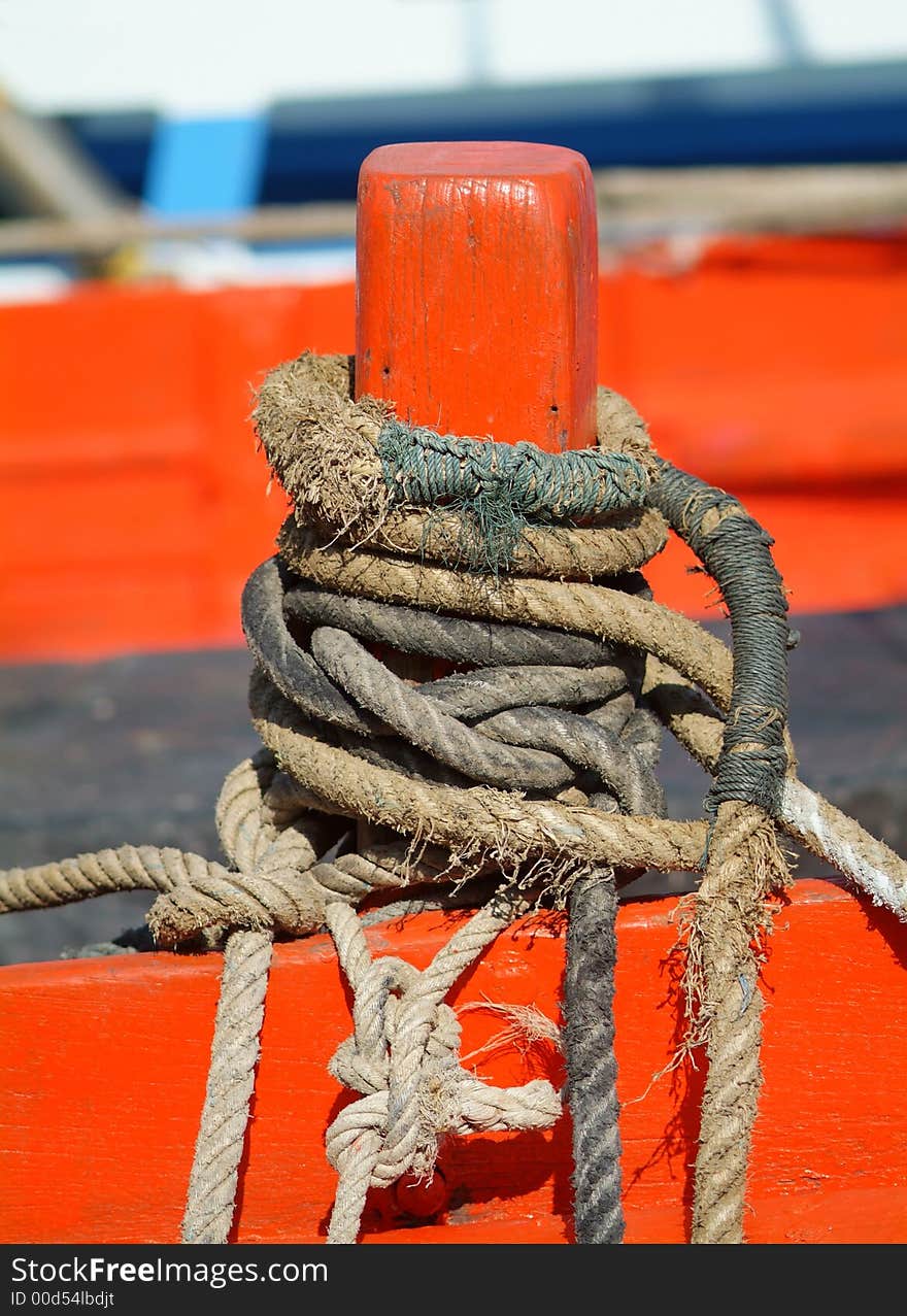 Several old, worn ropes on an orange cleat at a wooden boat.