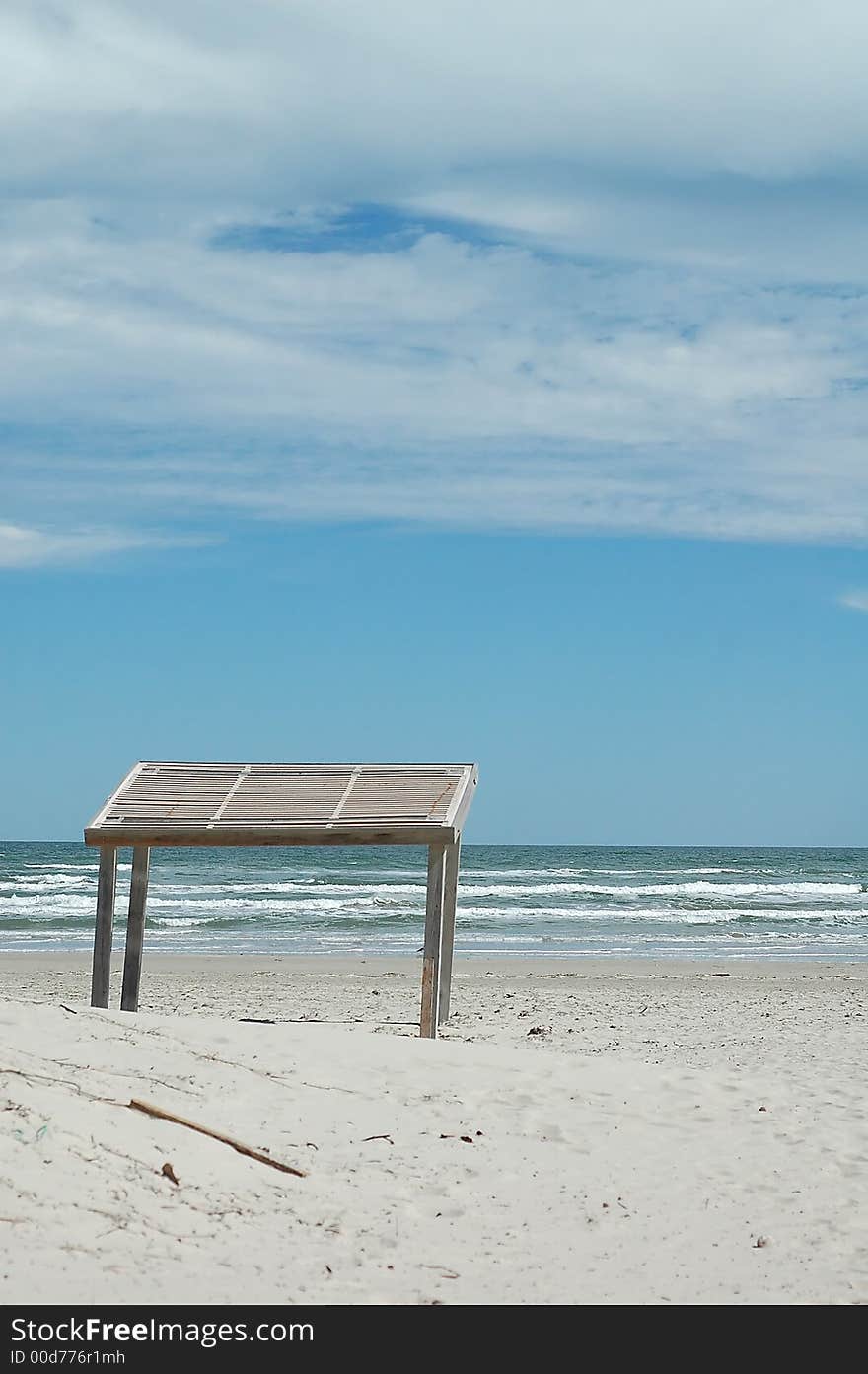 A white sand beach with a blue sky and cabana on the background