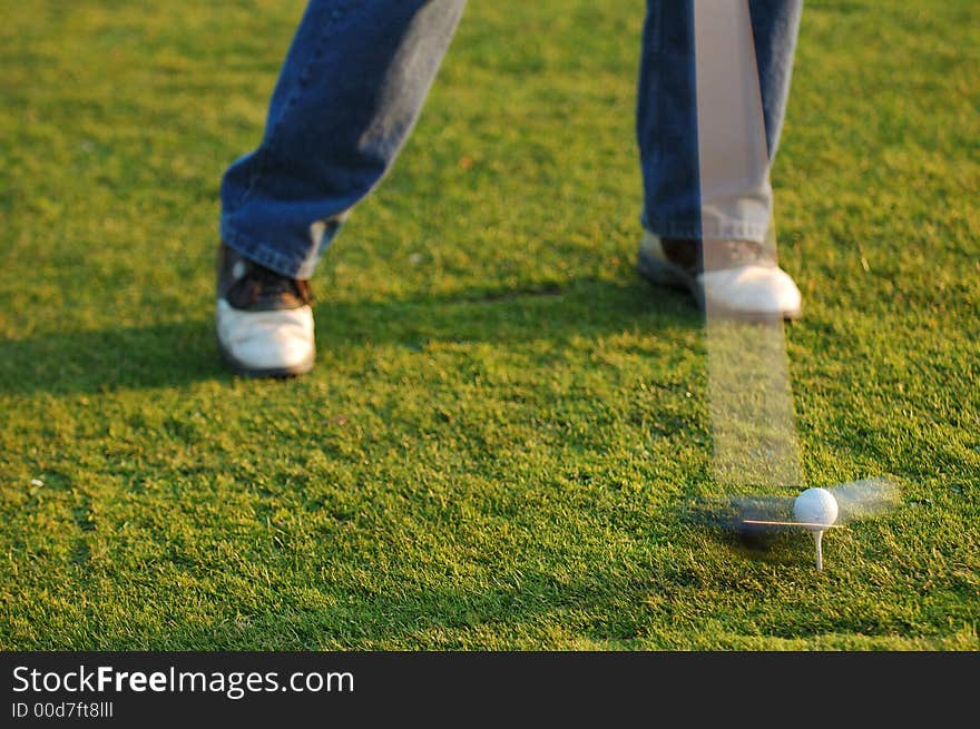 Golfer in swing as head of club hits ball in motion demonstrating the speed of the head of the club. Golfer in swing as head of club hits ball in motion demonstrating the speed of the head of the club