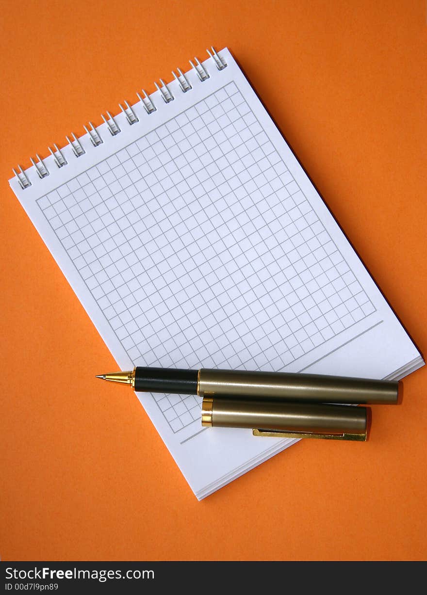 Notebook with a spiral with a place for the text and a pen on an orange background. Notebook with a spiral with a place for the text and a pen on an orange background.