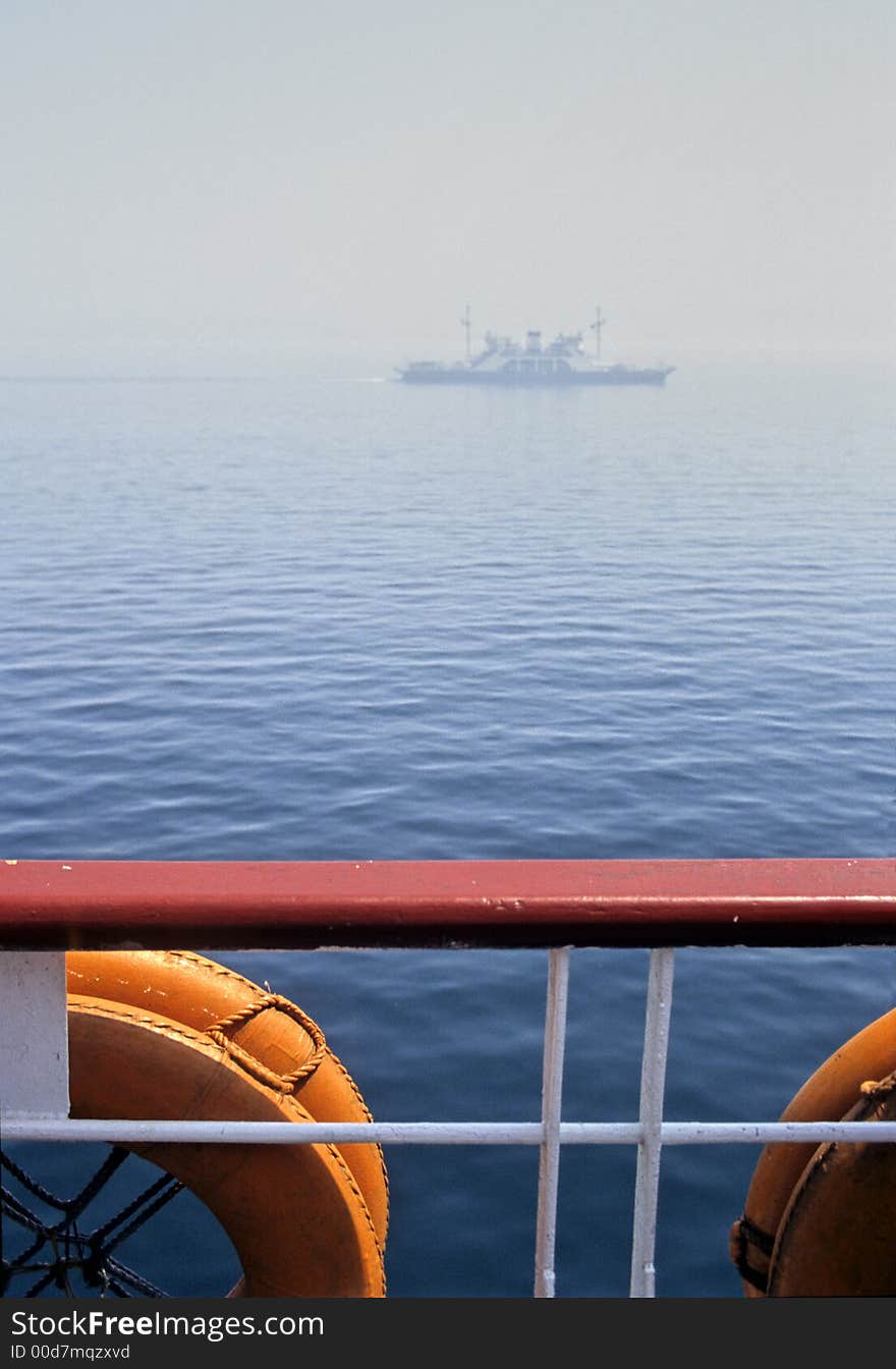 Boat rail and lifebuoys as foreground, boat in the fog as background showing navigation security problems. Boat rail and lifebuoys as foreground, boat in the fog as background showing navigation security problems.