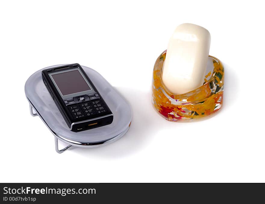 Bar of soap in cellphone holder and cellphone in soap dish isolated over white background. Bar of soap in cellphone holder and cellphone in soap dish isolated over white background