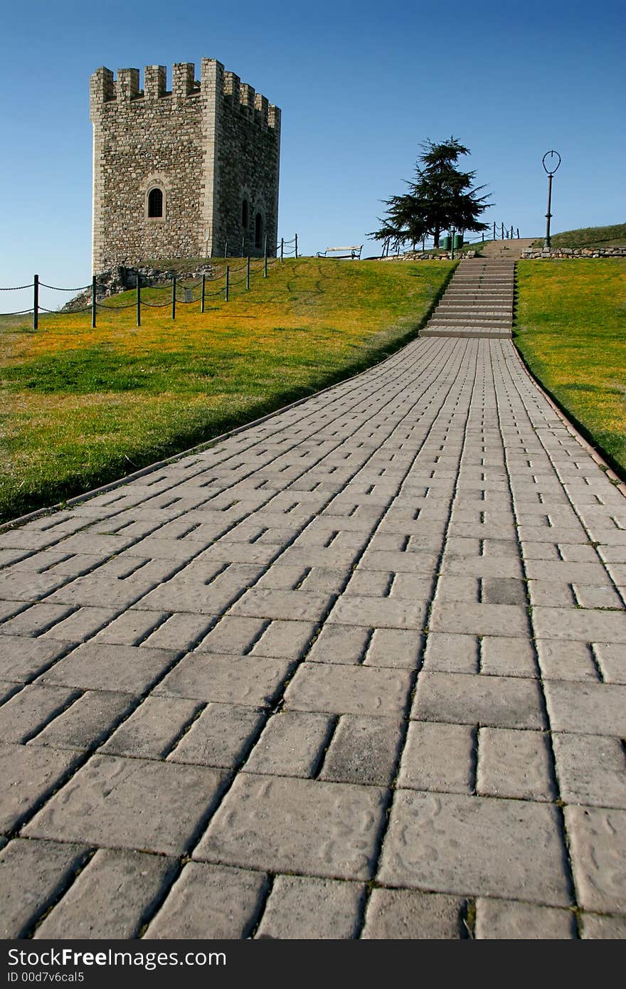 A tower along a stone road with green/yellow grass and a clear blue sky. A tower along a stone road with green/yellow grass and a clear blue sky.