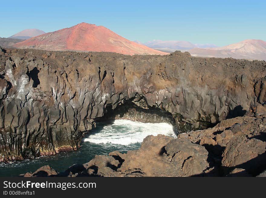 Volcanic rocks by the water and red montain. Volcanic rocks by the water and red montain