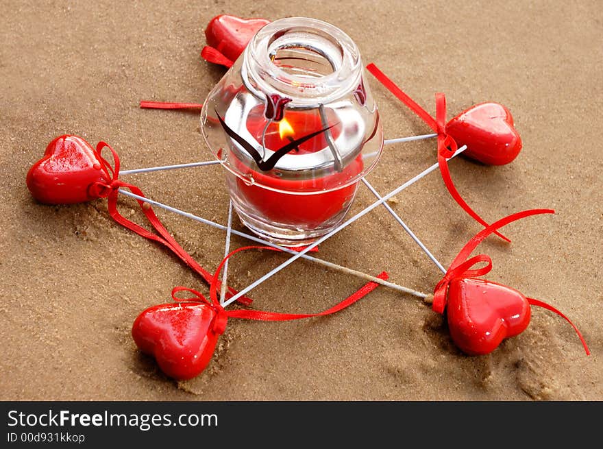Five pointed star made from red hearts and a burning candle on sand conceptual still life. Five pointed star made from red hearts and a burning candle on sand conceptual still life