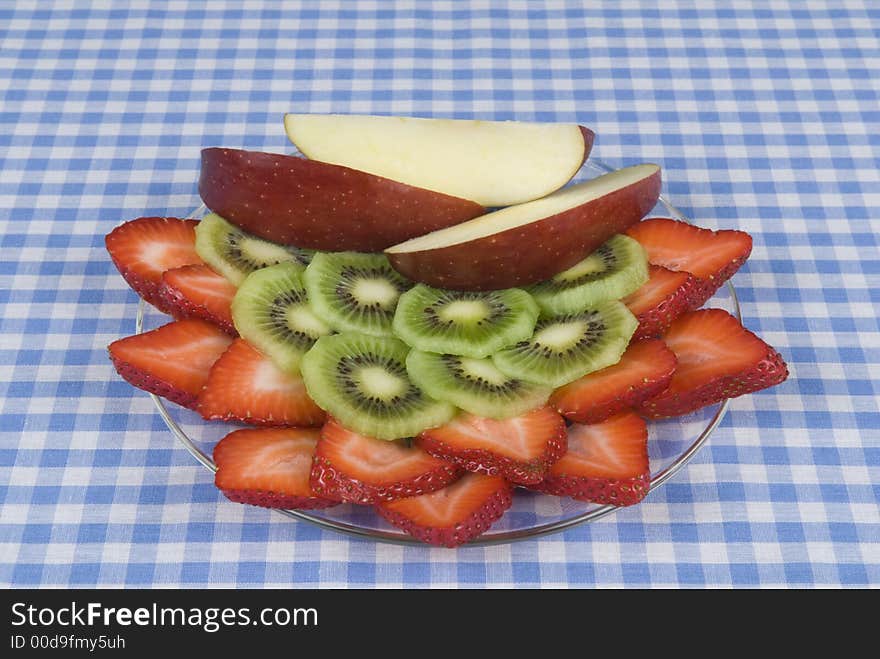 Apples, strawberry, kiwi fruit dish on a blue and white checkerboard cloth