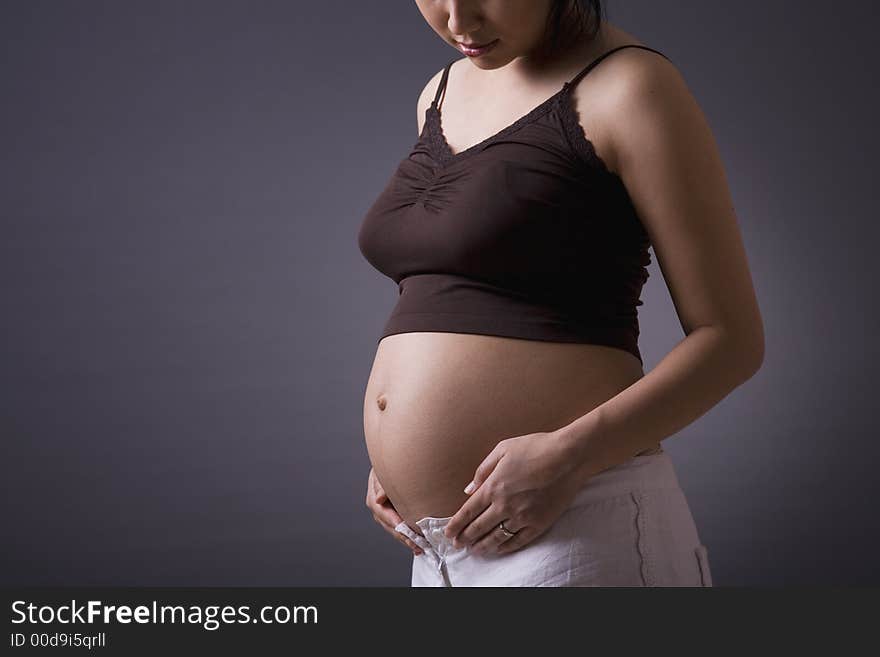 Studio shot of a pregnant woman standing over grey background with her stomach exposed. Studio shot of a pregnant woman standing over grey background with her stomach exposed