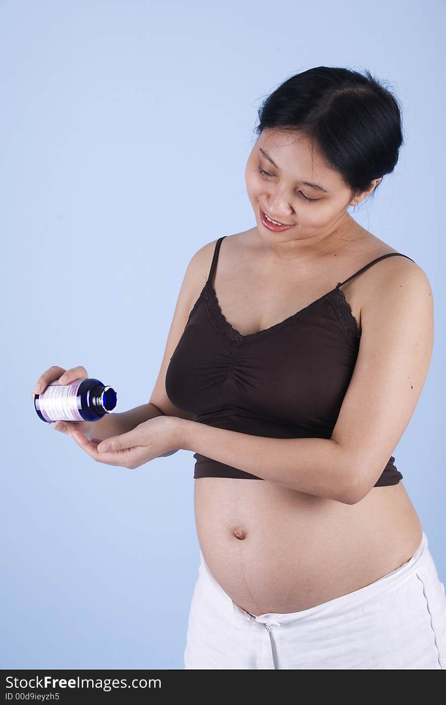 Studio shot of a pregnant woman taking vitamin over blue background with her stomach exposed. Studio shot of a pregnant woman taking vitamin over blue background with her stomach exposed