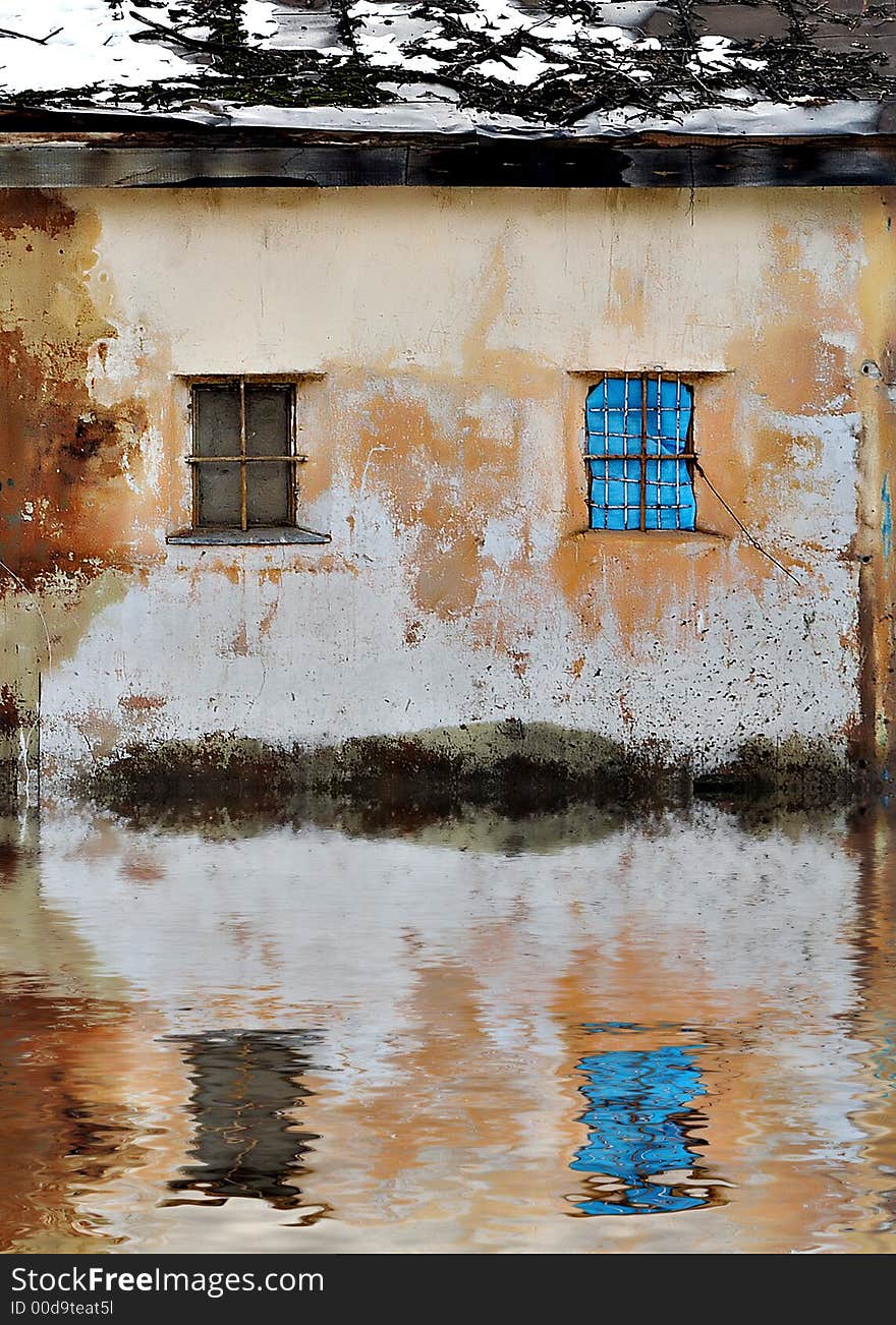 Ragged wall of a house with two windows and the water which has spread near it during spring flooding. Ragged wall of a house with two windows and the water which has spread near it during spring flooding