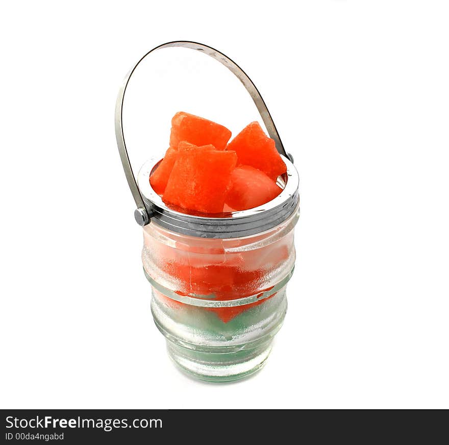 Red ice cubes put in a glass jug with metal handle, view from above on the white background