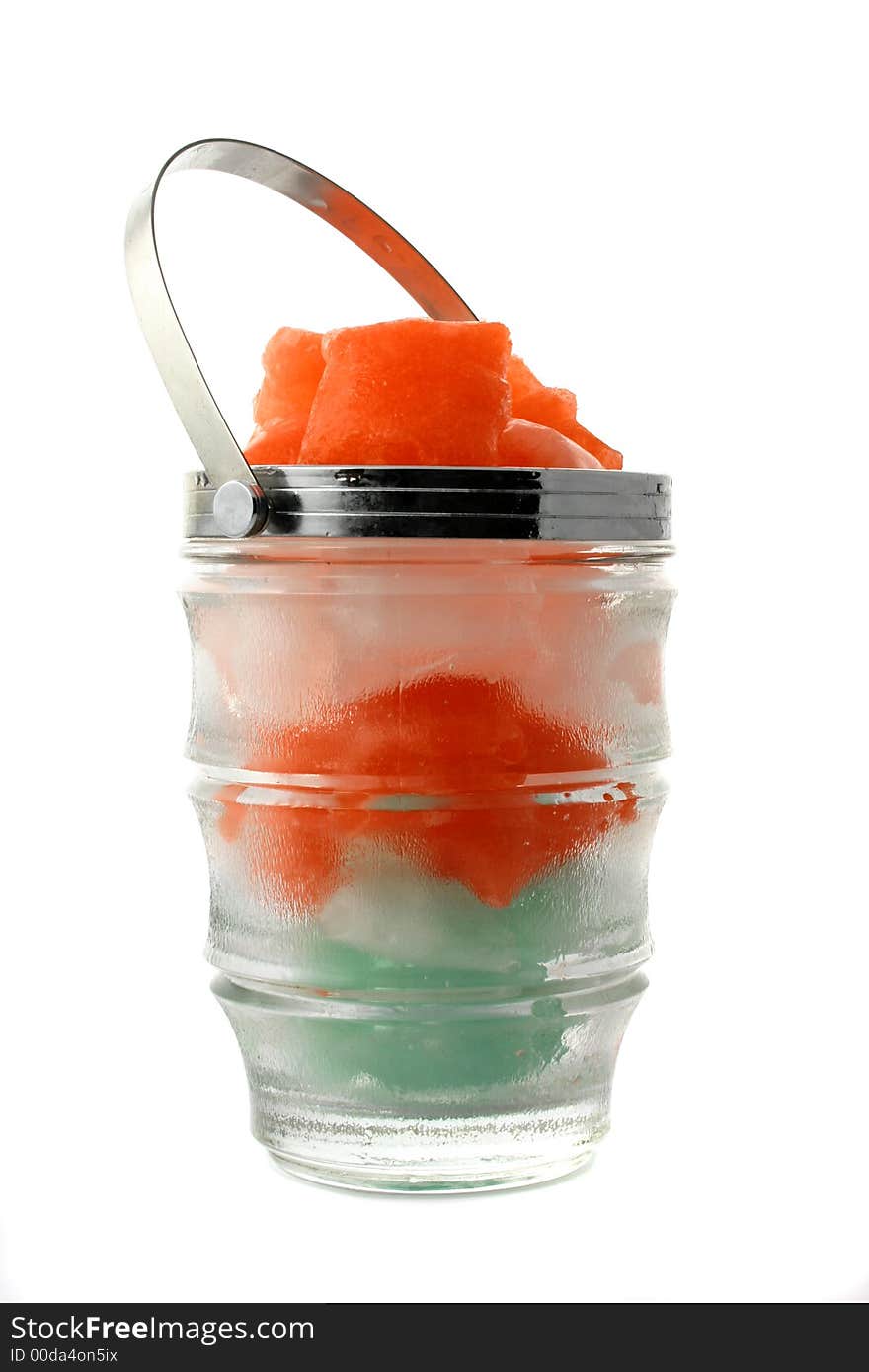 Green, red and white ice cubes put in a glass jug with metal handle on the white background. Green, red and white ice cubes put in a glass jug with metal handle on the white background