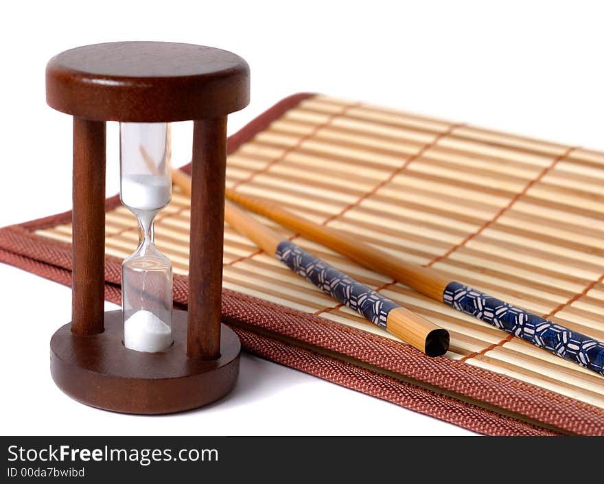 Composition of chopsticks, sand glass and bamboo table-cloth over white background. Composition of chopsticks, sand glass and bamboo table-cloth over white background