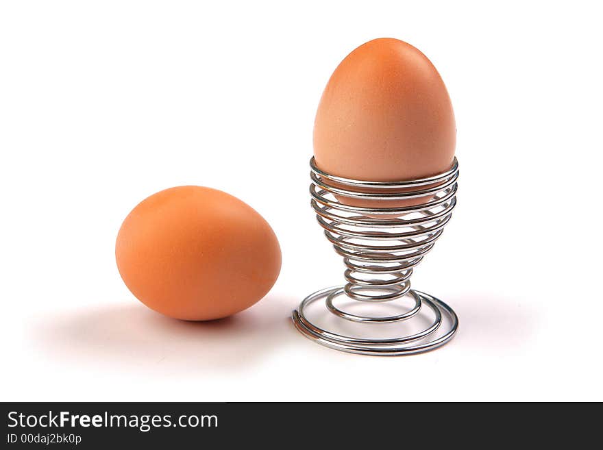 One egg in metal holder and one egg beside that, on white background. One egg in metal holder and one egg beside that, on white background