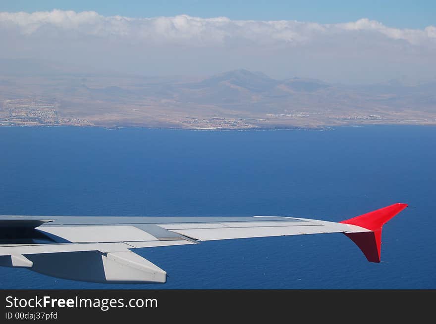 Airplane wing against blue ocean and the island of Fuerteventura, aerial view. Airplane wing against blue ocean and the island of Fuerteventura, aerial view.