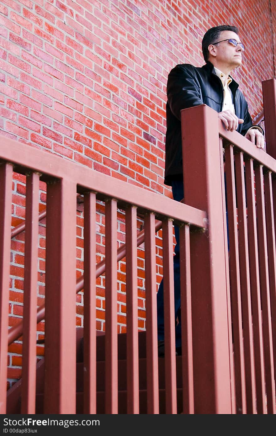 Man standing on the steep stair case of a large red brick building thoughtfully surveying his surroundings. Man standing on the steep stair case of a large red brick building thoughtfully surveying his surroundings.