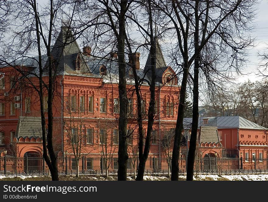 Ancient building from a red brick close up in the late winter with trees in the foreground and the dark blue cloudy sky - on back