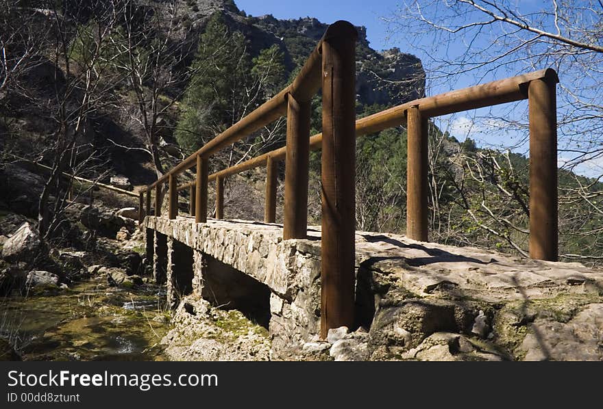 A bridge made of stone and wood crossing a river in a forest. A bridge made of stone and wood crossing a river in a forest