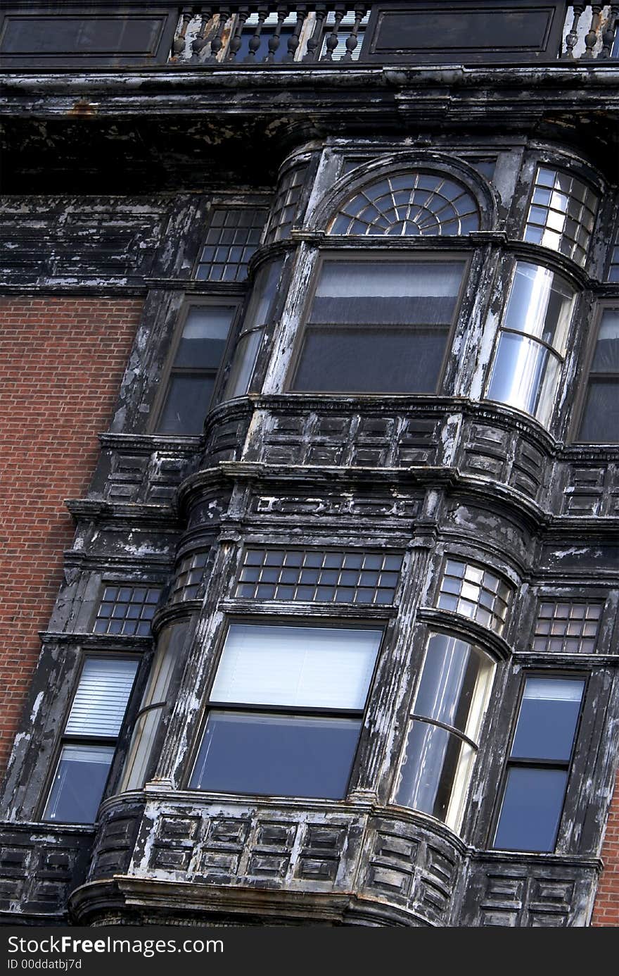 Detail of old bowed windows on brownstone building in boston, smaller windows have many panes, shade is puled half way down