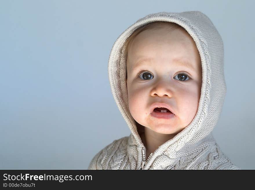 Image of cute baby wearing a hooded sweater, sitting in front of a white background. Image of cute baby wearing a hooded sweater, sitting in front of a white background