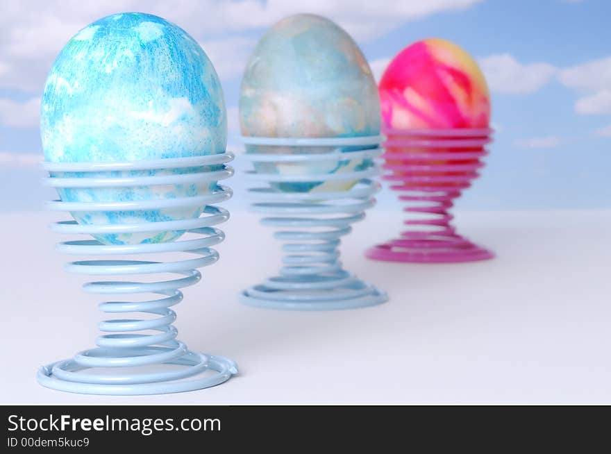 Three Decorated Easter Eggs on Coil Springs against a Blue Sky with Clouds