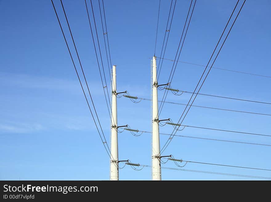 Two white electricity pylons, and wires stretching against the blue sky. Two white electricity pylons, and wires stretching against the blue sky.