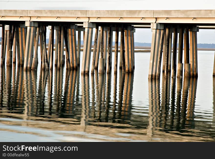 Bridge supports reflected in water with warm light from sunset