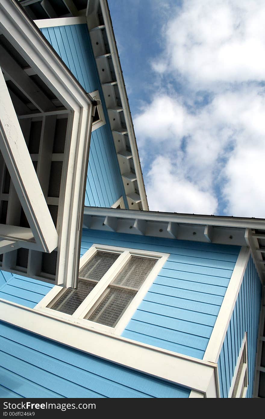 Upward view of corner of beach house against blue sky with white clouds. Upward view of corner of beach house against blue sky with white clouds