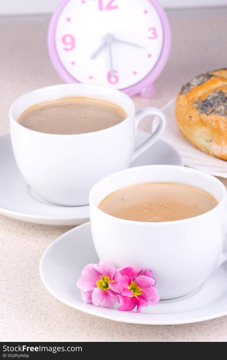 Two cups of coffee with clock and bread in the background. Two cups of coffee with clock and bread in the background.