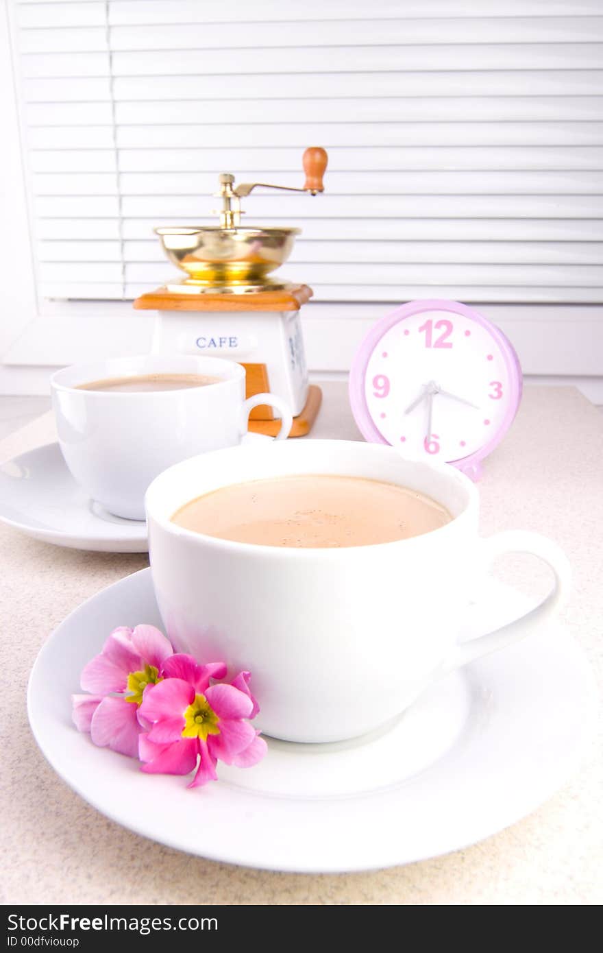 Two cups of coffee with a coffee-mill and clock in the background. Two cups of coffee with a coffee-mill and clock in the background.