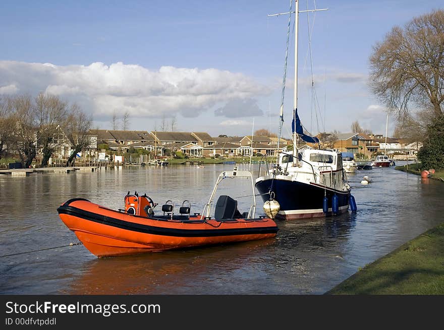 Red dinghy and boat moored on river bank on a sunny afternoon