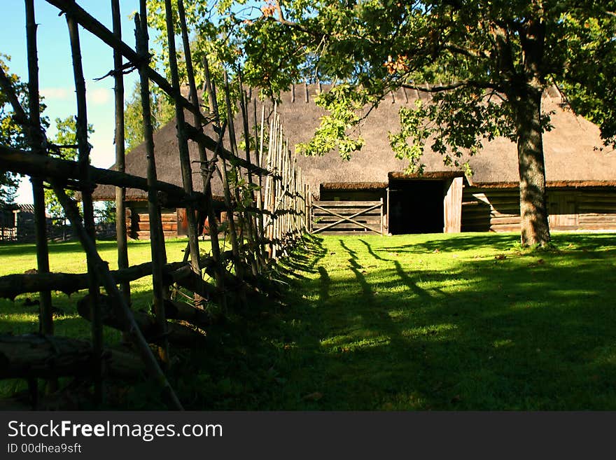 Old curve fence and greater log hut with a straw roof. Old curve fence and greater log hut with a straw roof