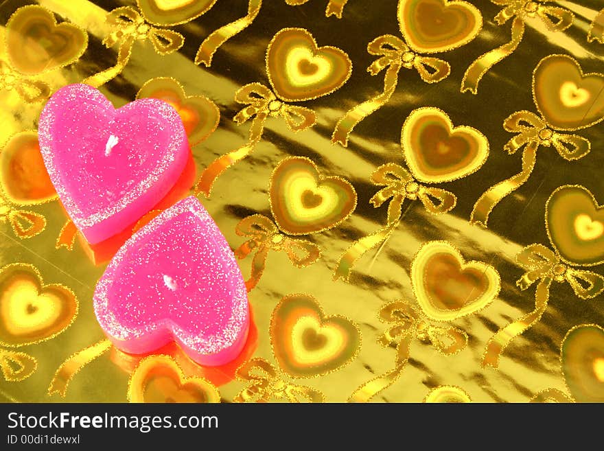 Two candles in the form of hearts on a golden background