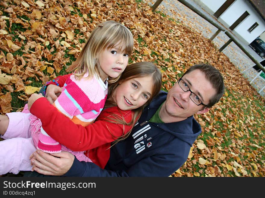 Father with his two daughters sitting in a park in autum leaves. Father with his two daughters sitting in a park in autum leaves