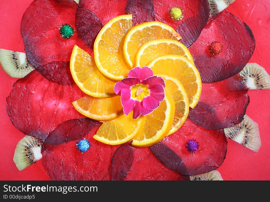 Arrangement of slices of beetroot and orange,with a flower in the middle and pieces of Kiwi,on a glass-plate with a red rim