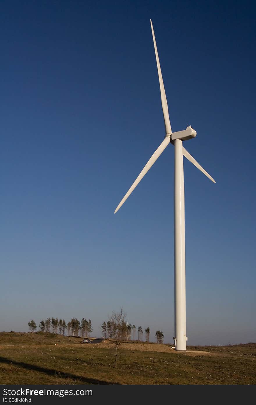 Aerogenerator with a set of trees on the horizon over a blue sky. Aerogenerator with a set of trees on the horizon over a blue sky