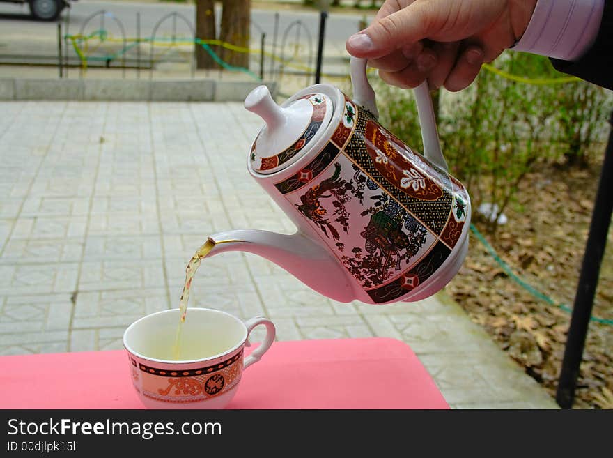 Pouring green tea in a teacup on a red table. Pouring green tea in a teacup on a red table