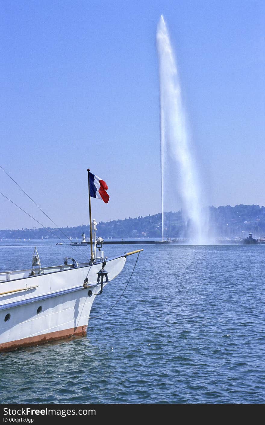 Famous Geneva water-jet on Leman lake with a boat under french flag as foreground. Famous Geneva water-jet on Leman lake with a boat under french flag as foreground.