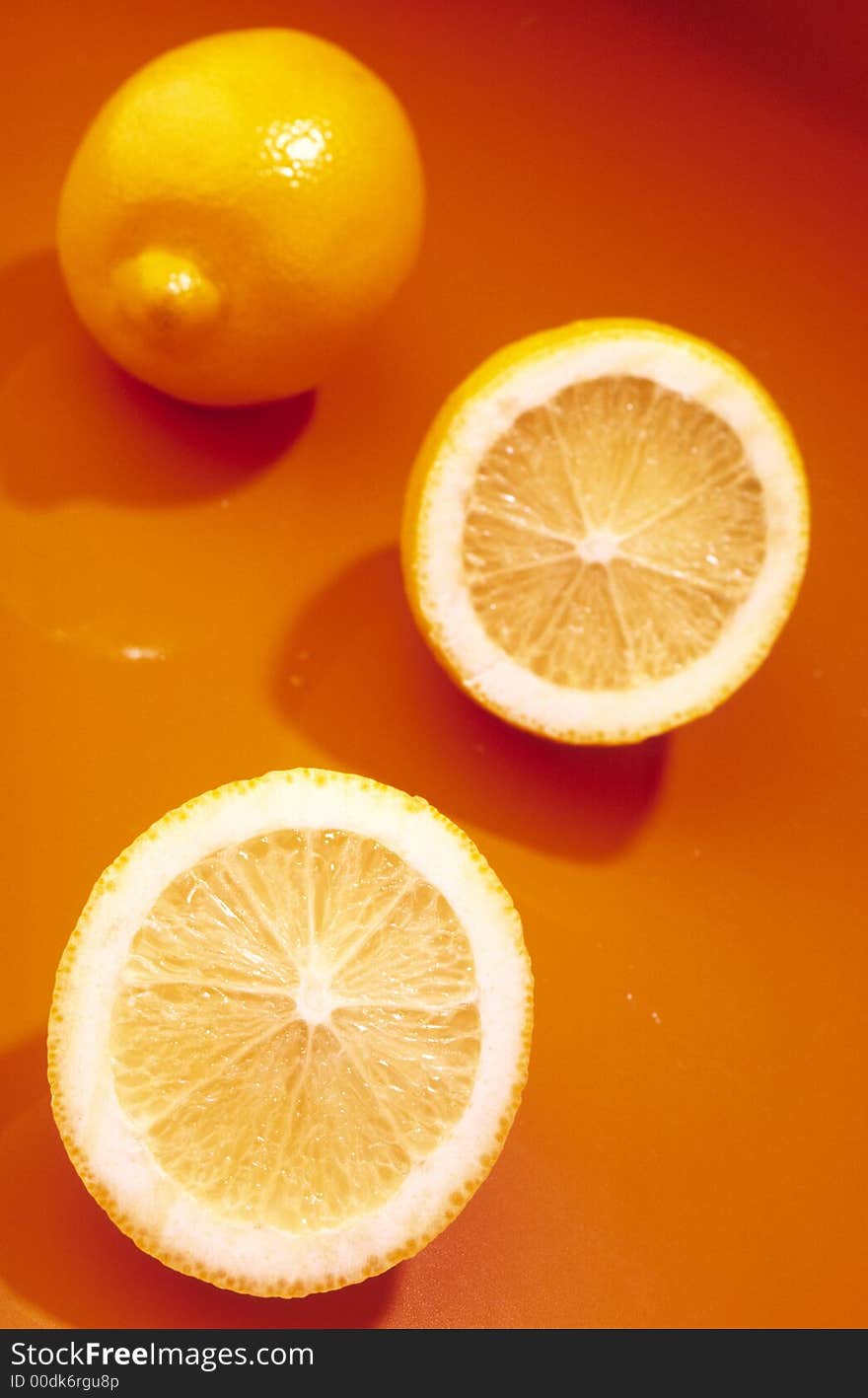 Whole yellow lemon and two slices of lemon on an orange background