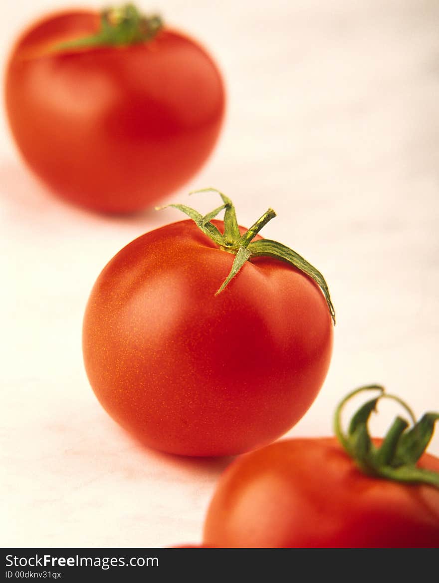 Three red tomatoes with green leaves on white background