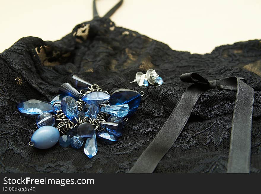 Blue bracelet and earrings lying on black see-through lace lingerie with satin ribbon.