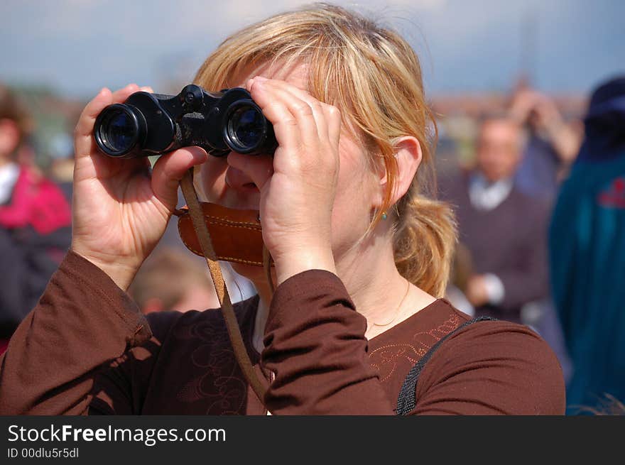 Woman with binoculars observing distant events, surrounded by crowd. Woman with binoculars observing distant events, surrounded by crowd.