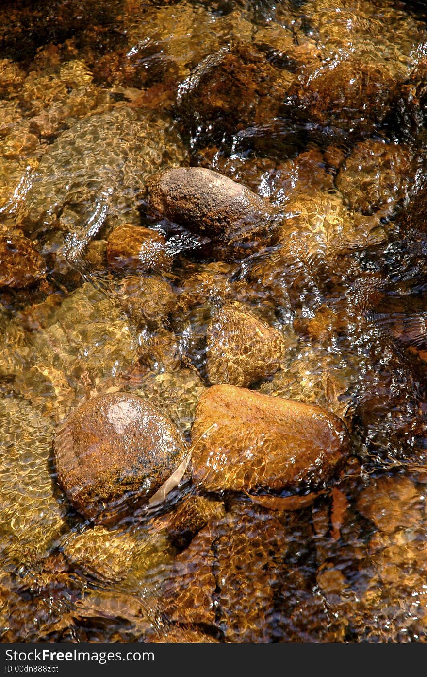 The crystal clear running water over the rocks of a mountain creek bed with gilmmering reflections from the sun in it