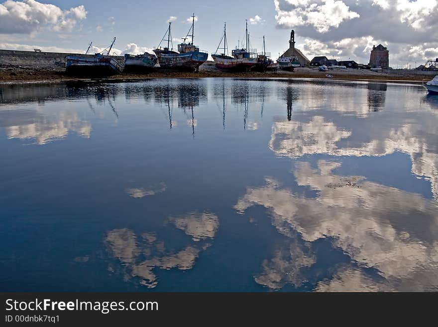 Blue water reflecting the clouds, with old harbor and boat silhouettes. Blue water reflecting the clouds, with old harbor and boat silhouettes