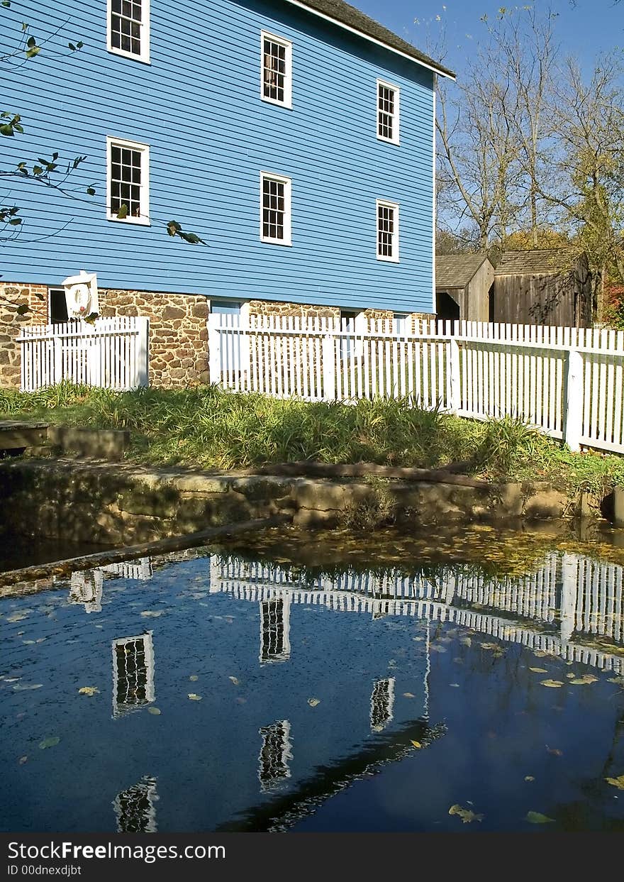 A historic blue mill reflects off the water. A historic blue mill reflects off the water.