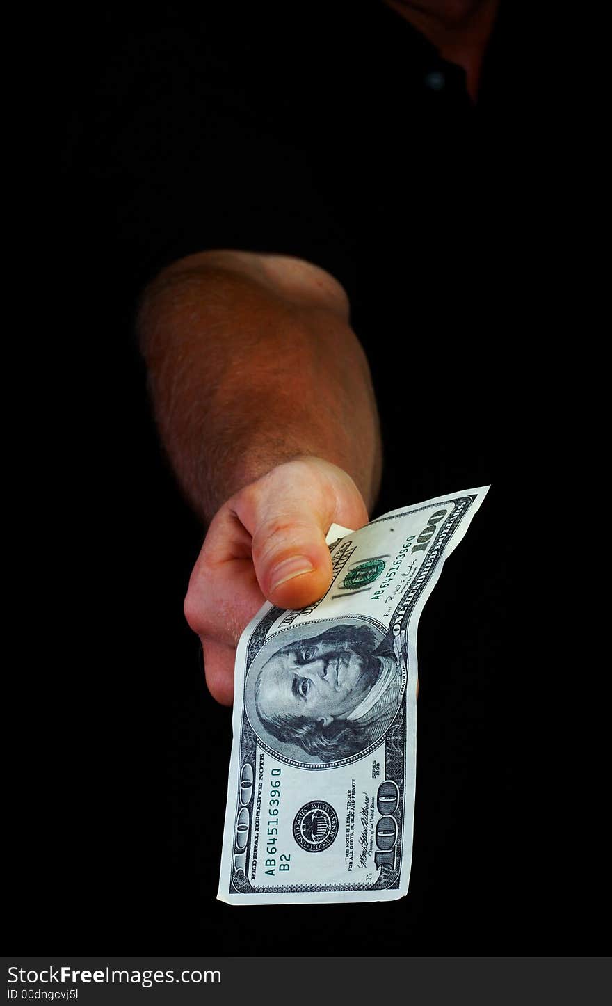 View of man’s hand coming out from the dark with a hundred dollars bill