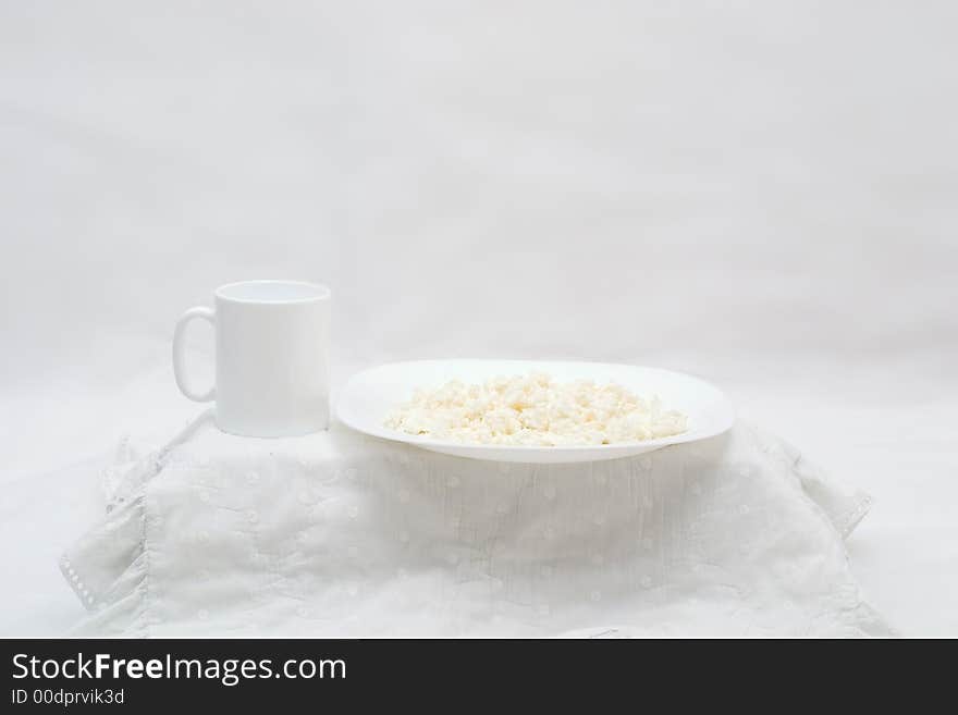 White table with curd on white plate and white cup on the white background. White table with curd on white plate and white cup on the white background