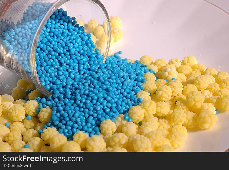 Small blue candies in a small glass on a saucer with yellow candies