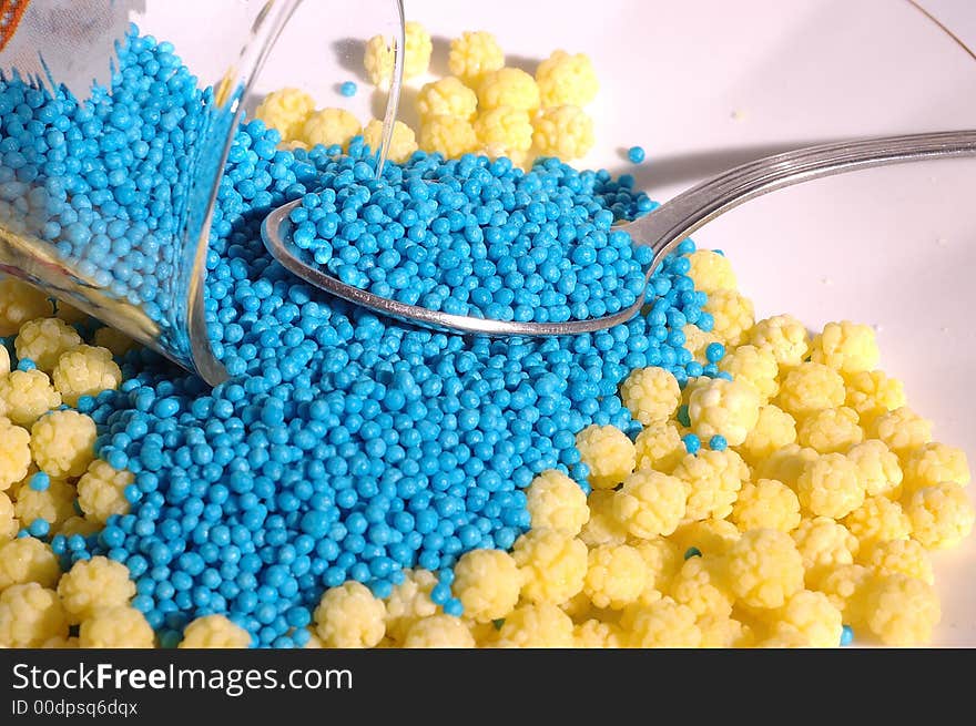 Small blue candies in a small glass on a saucer with yellow candies and teaspoon